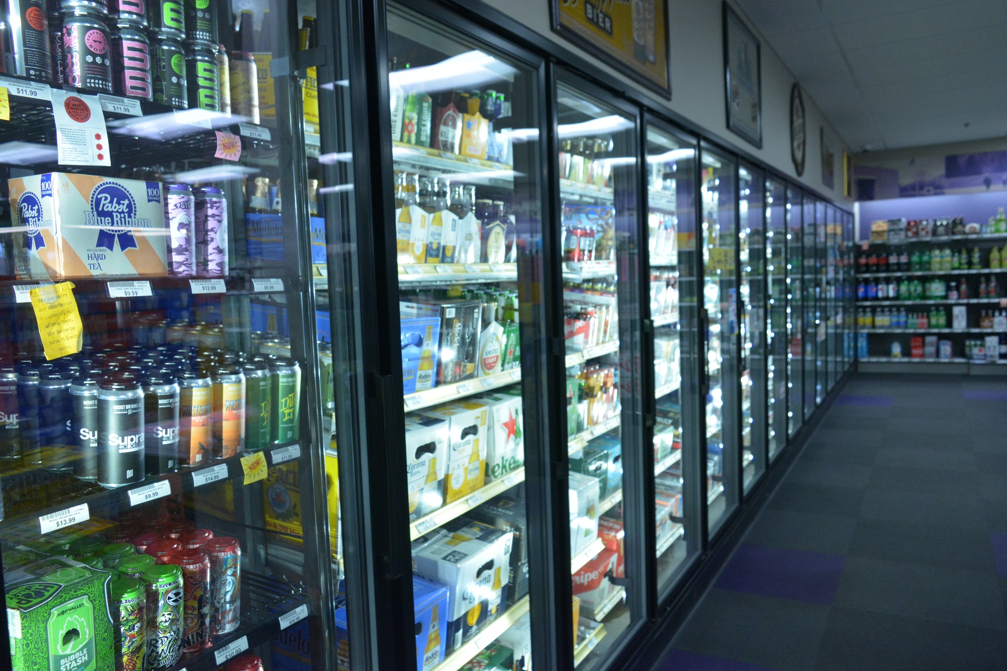 A long row of glass-door refrigerated coolers filled with various beers and canned beverages in a liquor store.