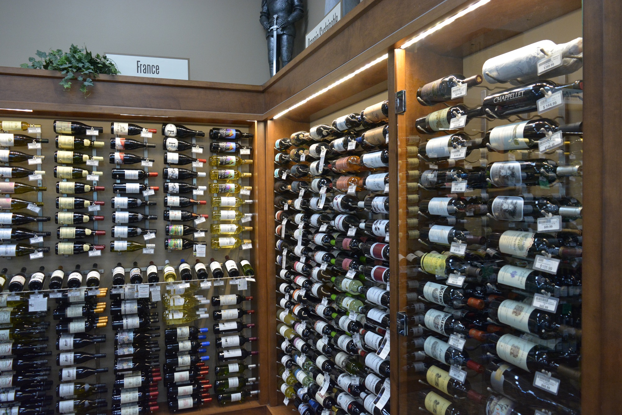 Premium wine cellar at Apple Valley Liquor featuring back-lit wooden racks and a knight in armor display.